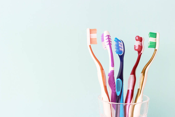 Veelkleurige tandenborstels in een glazen beker, blauwe achtergrond - Foto, afbeelding