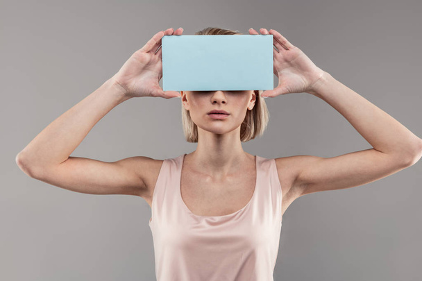 Resolute skinny woman with bob haircut placing blue cardboard on her face - Φωτογραφία, εικόνα