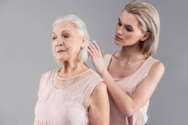 Attentive young blonde girl correcting hairstyle of her old mother - Foto, Imagem