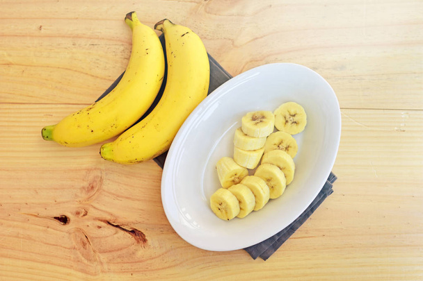 Draufsicht auf eine Schüssel mit geschnittenen reifen Bananen auf hölzernem Hintergrund. - Foto, Bild