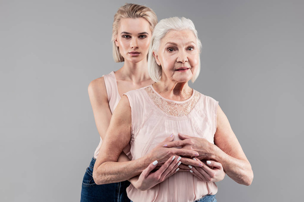 Suspicious good-looking fit girl connecting hands with her senior mother - Foto, Imagen