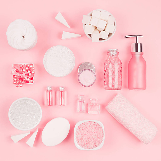Natural skin care products, accessories for bathroom - cream, salt, essential oil, soap, towel, perfume, pearls, gift, box, bottles, bowl on pink background, sqaure. - Photo, Image