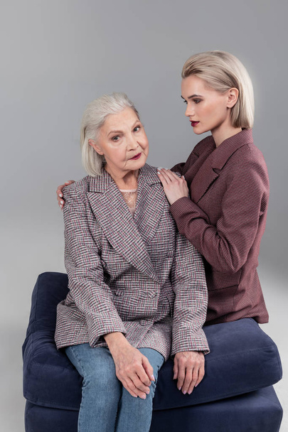 Serious senior grey-haired woman sitting on velvet sofa with her daughter - Photo, Image