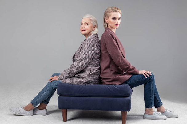 Resolute serious women sitting on blue sofa back to back - Valokuva, kuva