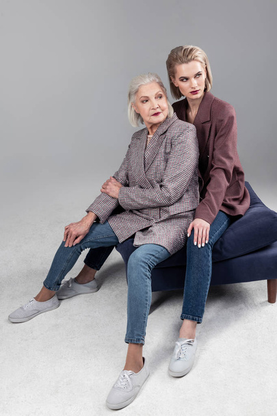 Active senior grey-haired mother sitting between legs of her beautiful daughter - Foto, imagen