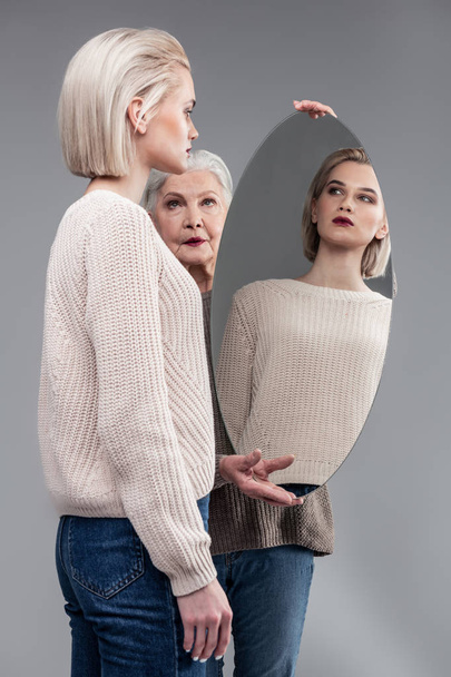 Grey-haired serious mother carrying round mirror while her daughter - Fotografie, Obrázek