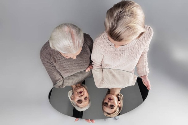 Легкошерсті допитливі жінки в легких в'язаних светрах дивиться у дзеркало
 - Фото, зображення