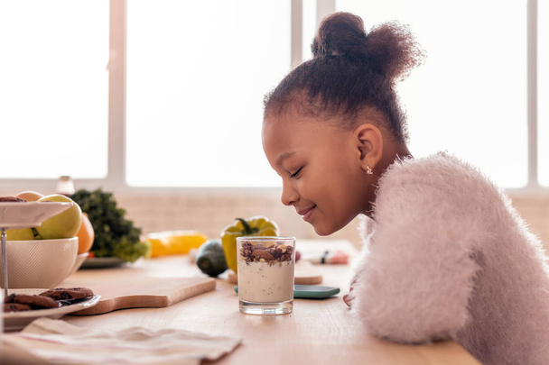 Curly African-American girl looking at sweet pudding with nuts - Fotografie, Obrázek