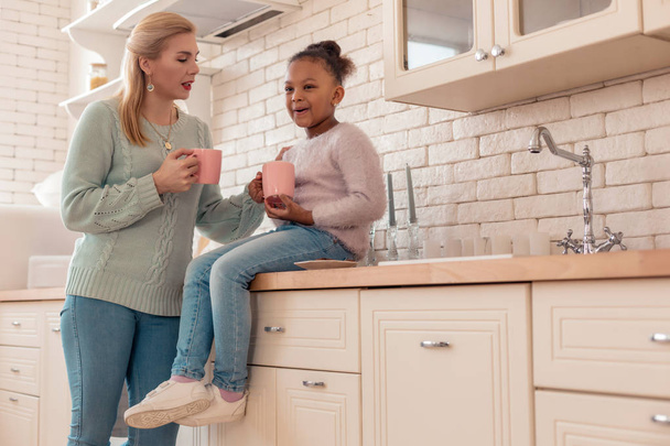 Mother and daughter drinking morning tea in the kitchen together - Photo, Image
