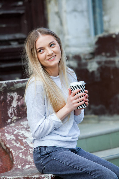 Tyylikäs hipster tyttö juo kahvia street.Outdoor muoti muotokuva nuori kaunis tyttö juo kahvia go.Close up muotokuva hymyilevä nuori tyttö tilalla ottaa pois kahvikupin ulkona
. - Valokuva, kuva