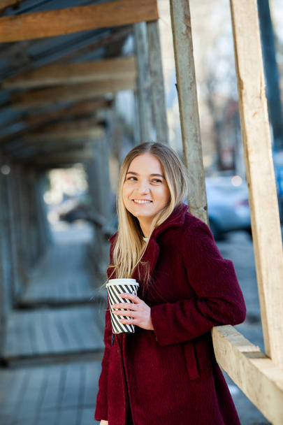 Outdoors fashion portrait of young beautiful girl drinking coffee to go.Close up portrait of a smiling young girl holding take away coffee cup outdoors.Beautiful woman holding paper coffee cup in the city - Photo, Image