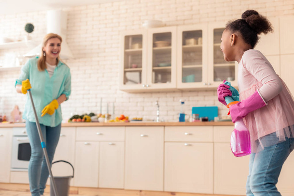 Cute curly daughter having much fun helping her mom with cleaning - Photo, Image