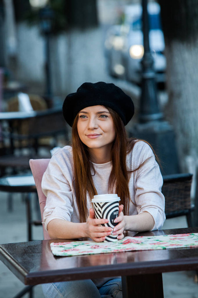Outdoors fashion portrait of young beautiful girl drinking coffee to go.Close up portrait of a smiling young girl holding take away coffee cup outdoors. - Фото, изображение