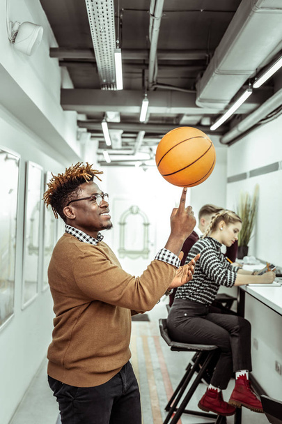 Smiling positive African American guy playing with basketball ball in office - Fotó, kép