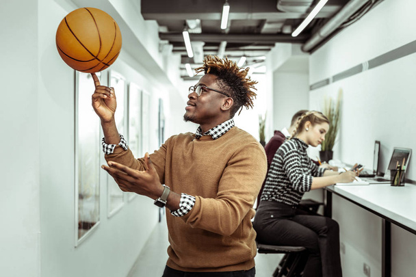 Active contented guy with dreadlocks rolling basketball ball on one finger - Foto, imagen