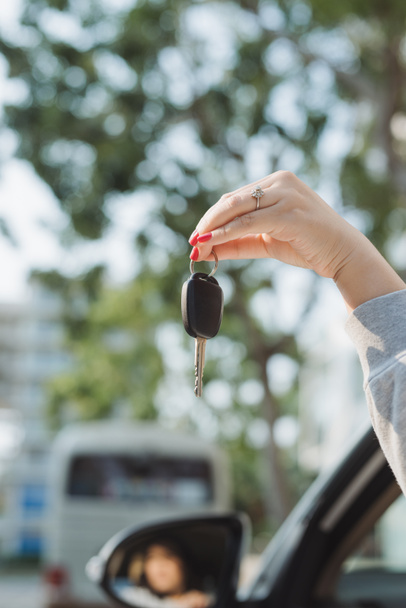 Frau hält Zündschlüssel eines Autos in der Hand, das durch die offene Seitenscheibe baumelt - Foto, Bild