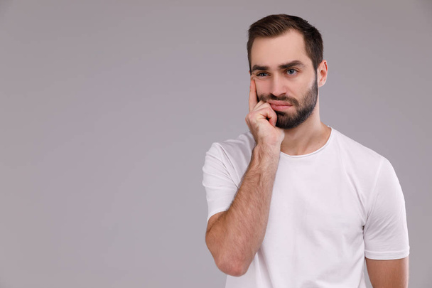 Portrait of a thinking man in a white T-shirt on a gray background. - Photo, image