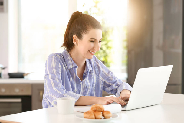Young female freelancer working with laptop in kitchen - Photo, Image