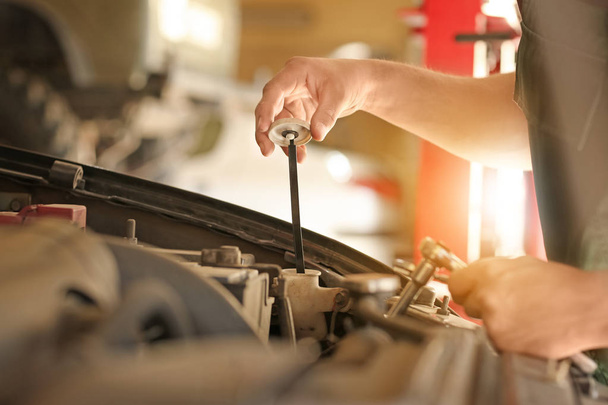 Молодой механик проверяет уровень масла в автомобильном сервисе
 - Фото, изображение
