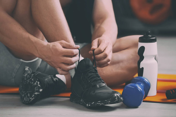 Young man tying shoelaces on floor in gym, closeup - Zdjęcie, obraz