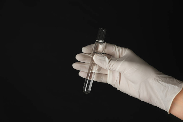 Работник лаборатории держит пробирку с водой на черном фоне
 - Фото, изображение