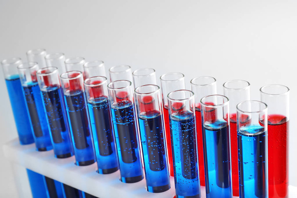 Tubos de ensaio com líquidos coloridos em suporte sobre fundo claro
 - Foto, Imagem