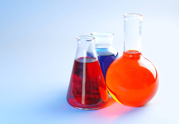 Chemiegläser mit unterschiedlichen Flüssigkeiten auf farbigem Hintergrund - Foto, Bild