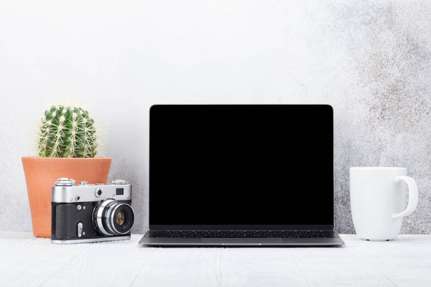 ufficio sul posto di lavoro con computer portatile vuoto, fotocamera e cactus su sfondo di pietra bianca
  - Foto, immagini