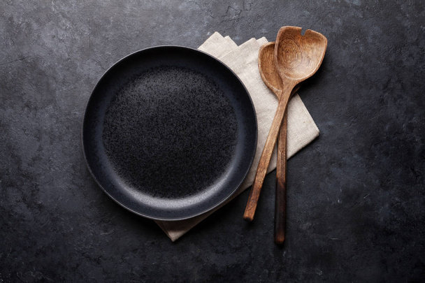 Ξύλινα σκεύη και άδειο πιάτο σε σκούρο φόντο πέτρα  - Φωτογραφία, εικόνα