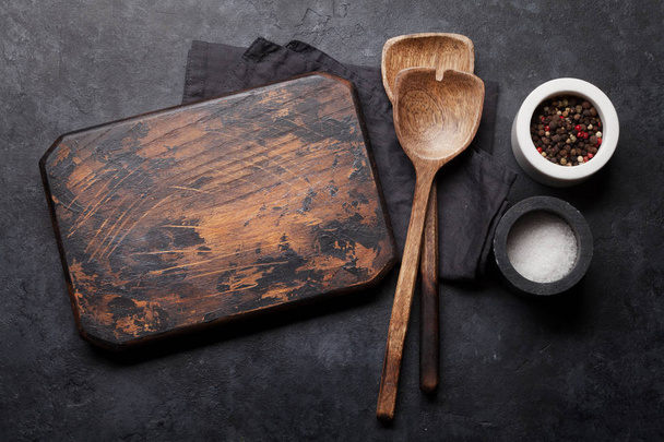 Kochutensilien aus Holz, Schneidebrett und Gewürze auf dunklem Steingrund  - Foto, Bild