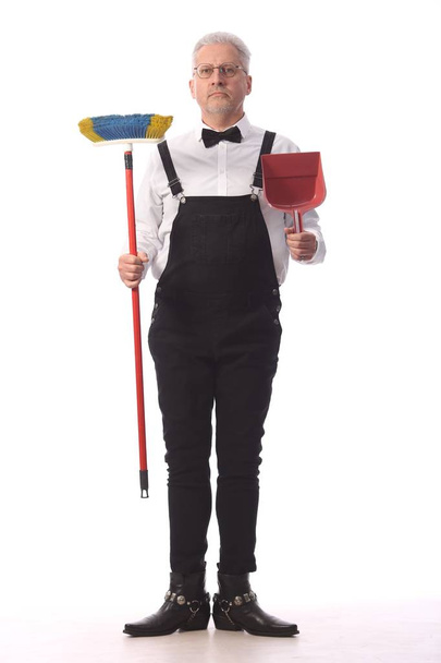 Gray-haired reiniger, conciërge in een zwarte jumpsuit met een mop en een Stofblik biedt schoonmaak service, op witte achtergrond - Foto, afbeelding