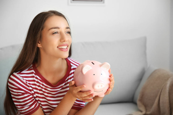 Young woman with piggy bank at home - Foto, immagini