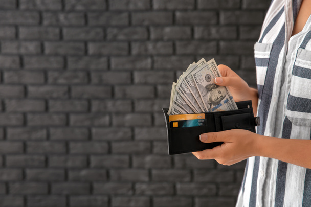 Молода жінка з гаманцем, повним грошей проти темної цегляної стіни, крупним планом
 - Фото, зображення