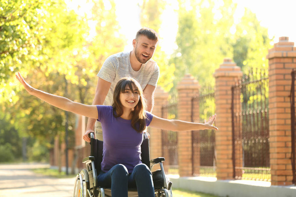 Gelukkig jonge vrouw in rolstoel en haar man buitenshuis - Foto, afbeelding