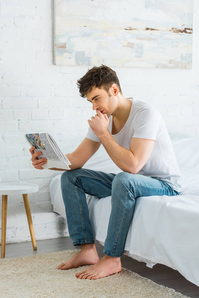 όμορφος άντρας κάθεται στο κρεβάτι και διαβάζοντας εφημερίδα στο σπίτι - Φωτογραφία, εικόνα
