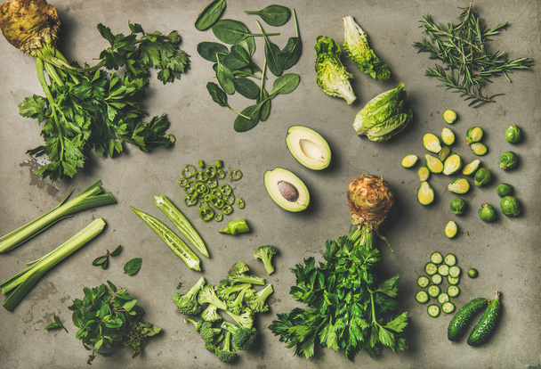Healthy vegan ingredients layout. Flat-lay of whole and cut green vegetables and edible herbs over concrete background, top view. Vegetarian, weight loss, raw, clean eating concept - Foto, Imagem