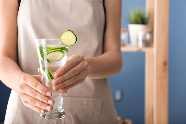 Woman holding glass with tasty fresh cucumber water indoors - Fotografie, Obrázek