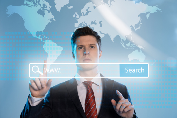 handsome businessman in suit pointing with finger at search bar in front on blue background - Photo, Image