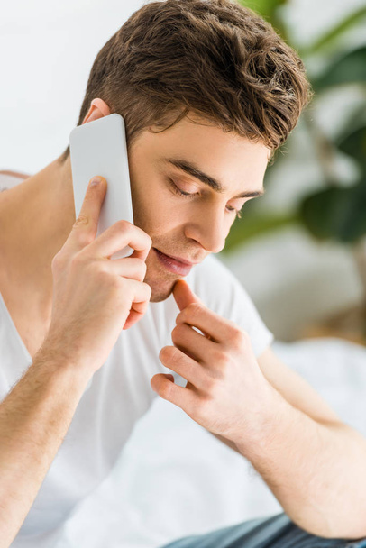selective focus of handsome man in white t-shirt talking on smartphone at home - Photo, Image