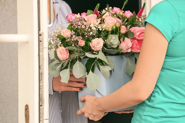 Young woman receiving gift box with beautiful flowers from courier - Foto, afbeelding