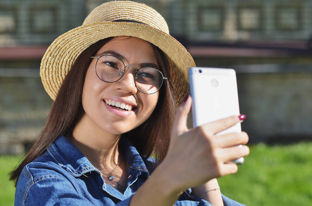 A girl in a straw hat and glasses takes a selfie on a Sunny spring day - Φωτογραφία, εικόνα