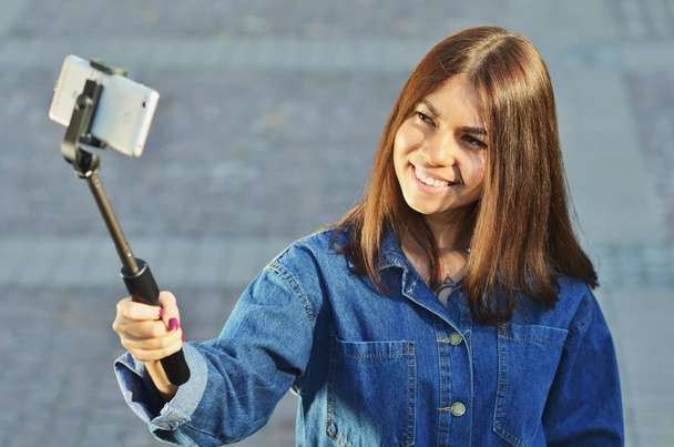 Brunette girl Asian looks in a denim suit takes a selfie and smiles - Фото, изображение
