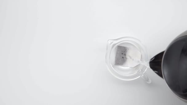 Pour hot water in glass kettle with tea bag on white background. Slow motion. Tea ceremony. Part 35. - Video