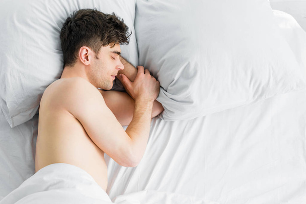 κάτοψη του όμορφος άνδρας κοιμάται στο κρεβάτι κάτω από την κουβέρτα με γυμνό τον κορμό στο σπίτι - Φωτογραφία, εικόνα