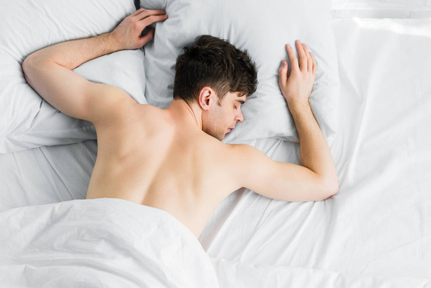 top view of handsome man sleeping under white blanket on bad - Fotografie, Obrázek