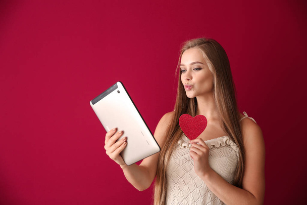 Mujer joven con Tablet PC que tiene citas en línea en el fondo de color
 - Foto, imagen