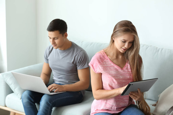Молода пара з ноутбуком і планшетним комп'ютером сидить на дивані вдома
 - Фото, зображення