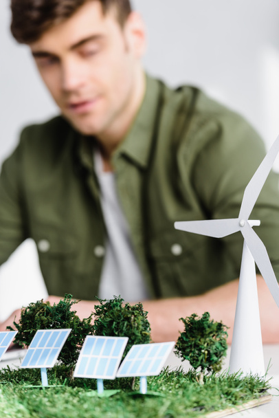 selective focus of architect at table with windmill, trees, solar panels models in office - Fotoğraf, Görsel