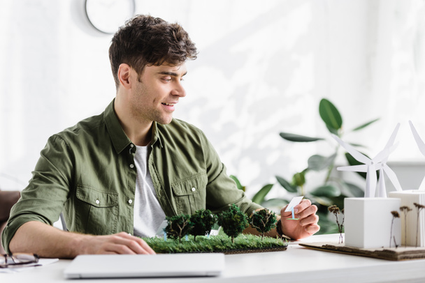 handsome architect holding solar panels models on grass near laptop in office - Photo, Image
