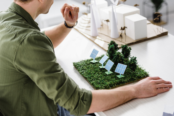 oříznutý pohled architekta sedí u stolu s modely stromů v úřadu a solární panely - Fotografie, Obrázek
